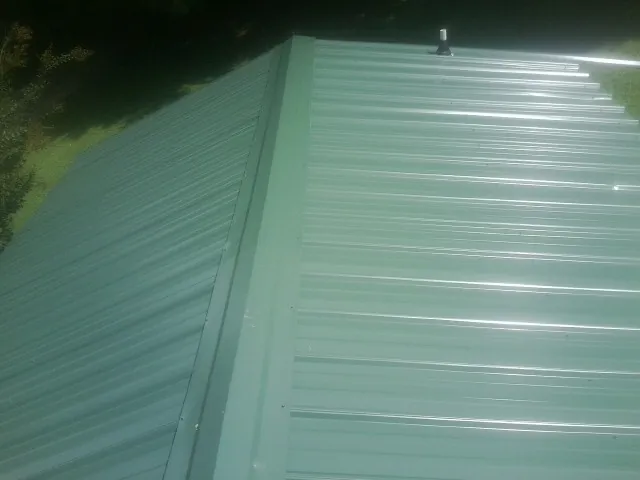New green metal panels meeting at the ridge of a roof — Flat Roof Repair work by our crew in Palmer